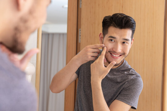 Young man smiling while squeezing pimple in mirror
