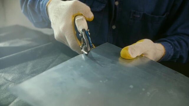 Professional metalworker wearing protective gloves using heavy duty scissors to cut a sheet of galvanized steel, demonstrating precision and skill in a workshop manufacturing setting