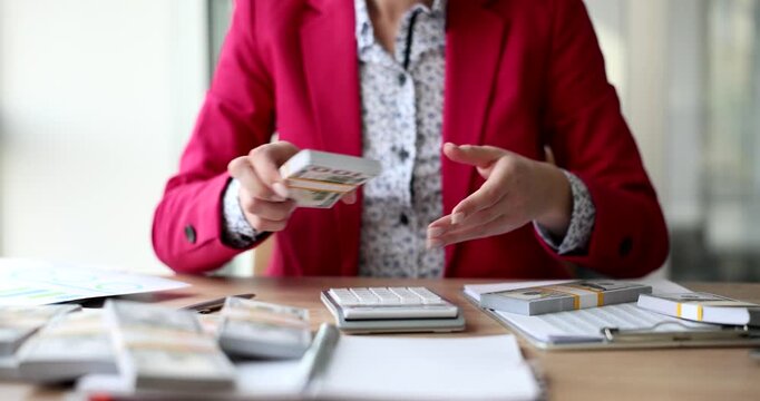 In a bright, contemporary workspace, a person in a red jacket counts cash and organizes bills. With papers and tools scattered on the table, focus is on careful money management.