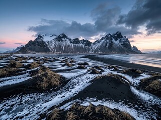Fototapeta premium Dramatic mountain peaks over black sand beach, snowy volcanic landscape at sunset, arctic coastal wilderness scenery