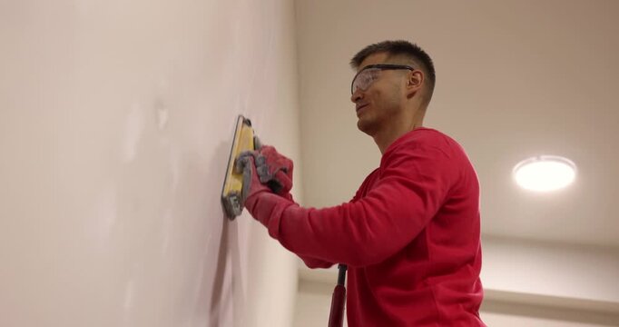 A skilled worker carefully smooths a wall with a sanding tool in a well-lit room. The bright space showcases his focus and precision while creating a flawless finish.