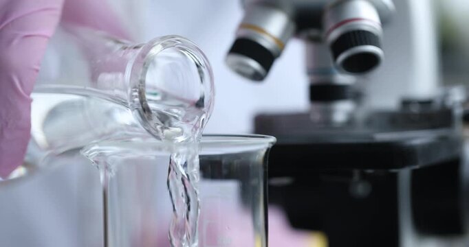 In a bright laboratory, a researcher skillfully transfers clear liquid from one container to another using careful techniques and scientific tools.