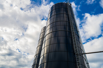 Tall metal farm silos against blue sky with white clouds on sunny day. © Octavian
