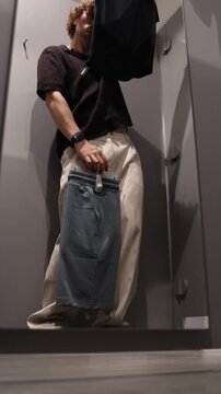 Vertical screen happy student dances with excitement while holding new clothes and celebrating a purchase after choosing his favorite outfit during a casual shopping trip