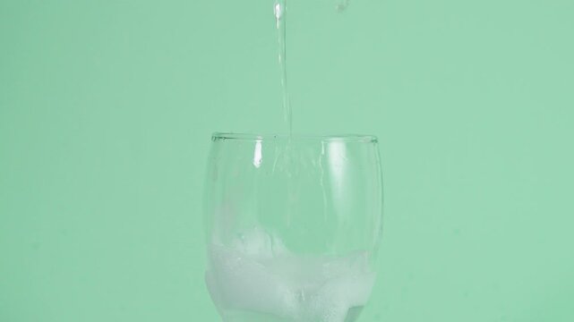   Close up of Water pouring into clear glass with soapy foam in green background