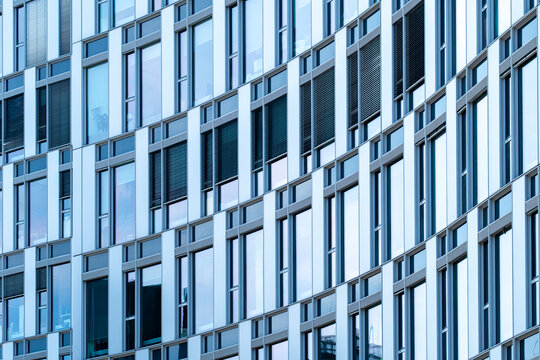 Modern building facade with repeating windows and blue glass panels forms a dense geometric architecture pattern across a contemporary urban exterior