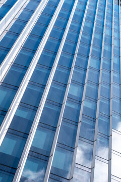 Blue glass facade with vertical windows on a modern building where reflective architecture and repeating lines create a clean abstract pattern filling the frame