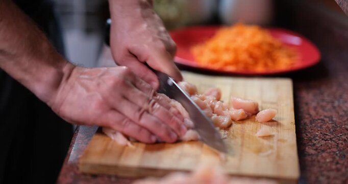 In a warm kitchen, hands skillfully chop fresh chicken on a wooden board alongside vibrant, diced vegetables. The inviting aroma promises a tasty dish to savor.