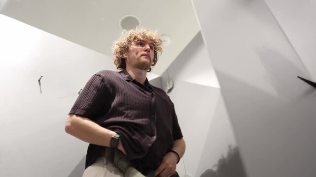 Man secretly hides a new garment under his arm while stealing clothes from a store fitting room showing suspicious behavior shoplifting and retail theft in public attempt