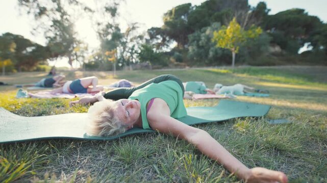 People stretch and relax on yoga mats in a park during a sunny day
