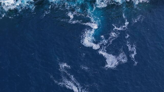 Aerial top down footage of Atlantic Ocean surface with rolling waves and white foam patterns. Drone view blue water with ripples and breaking waves for natural moving background