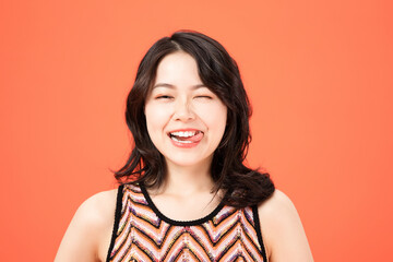Fototapeta premium Young woman playfully sticking tongue out and winking on orange background