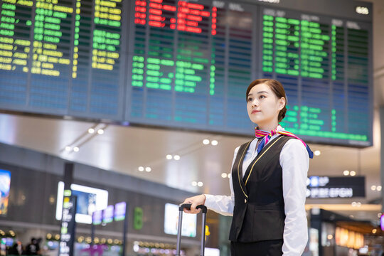 Asian flight attendant checking flight board at airport