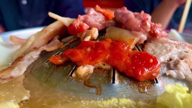 Close Up of Thai BBQ Moo Krata with Marinated Pork and Spicy Sauce on a Hot Grill