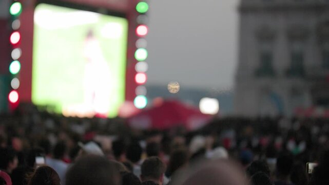 Crowd of diverse football fans watching championship match on large screen in Lisbon, with vibrant lights and festive atmosphere during the 2026 event