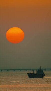 Sunset at the ocean with a ship sailing under the large sun in the sky