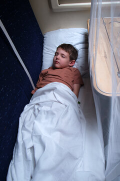 Sleeping child traveling in a train compartment. Young boy resting on a bunk bed in a passenger carriage. Comfortable railway transportation for a vacation journey and family tourism.