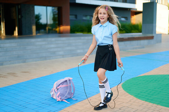 Happy schoolgirl jumping rope outdoors near school building