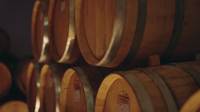 Wooden oak casks storing and aging red wine in a dark, underground cellar of a traditional winery, showcasing the rustic winemaking process and the production of alcoholic beverages