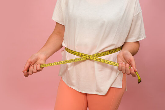 Woman measuring waist with yellow tape measure on pink background. Weight loss and diet control concept. Fitness slimming and healthy lifestyle for body measurement and progress