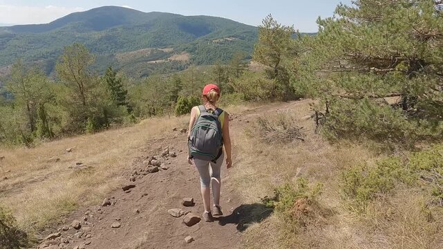 Fit senior woman carrying a backpack, in great shape and excellent physical condition, hiking on the mountain path. Concept of active aging and healthy lifestyle. 