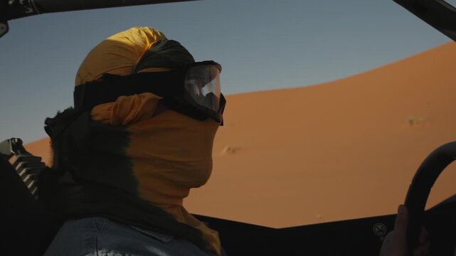 Desert off road adventure driver in headscarf and goggles gripping buggy steering wheel