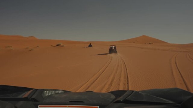 Driver view chasing buggy and quad bike over Sahara style sand dunes with tire tracks