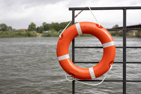 Orange lifebuoy on metal railing by water on cloudy day