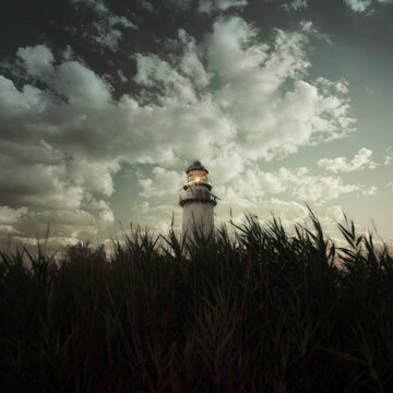 Moody Lighthouse Emerging From Reeds Under Stormy Sky