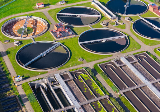 Aerial view of a wastewater treatment plant with circular sedimentation tanks, aeration basins, and green grass areas in Poland.