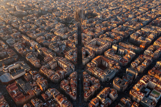 Aerial view of Sagrada Familia surrounded by the dense urban grid and historic rooftops of the Eixample district during golden hour Barcelona, Catalonia, Spain.