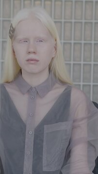 Slow motion portrait of beautiful albino woman in elegant clothes sitting in luxurious house looking at camera. Individual style and creative interior concept.