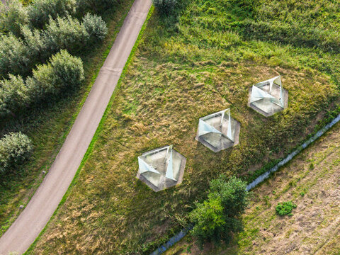Aerial view of three geometric glass installations at the RWZI Horstermeer facility, set in a grassy landscape beside a path in Nederhorst Den Berg, Noord-Holland, Netherlands.