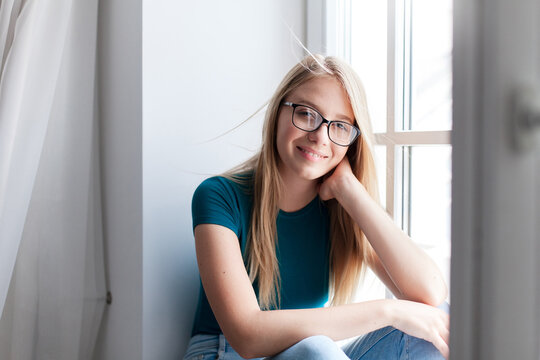 Young woman relaxing by window at home. Happy girl enjoying fresh air and cool wind. Concept of female mental health, slow living, mindfulness. Copy space