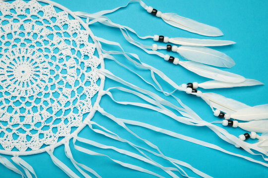 Handmade dream catcher hanging on a rope with feathers, threads, and beads on blue background.