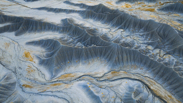 Aerial view of Factory Butte, showcasing its dramatic eroded badlands, intricate drainage patterns, and sparse yellow desert vegetation in Wayne County, Utah, United States.