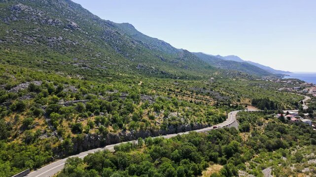 Winding road with cars, small villages and blue sea along rocky coast