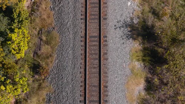 Parallel railroad tracks bordered by autumn woodland and grass in Gentry, Arkansas, aerial angled forward with shadow outline of trains