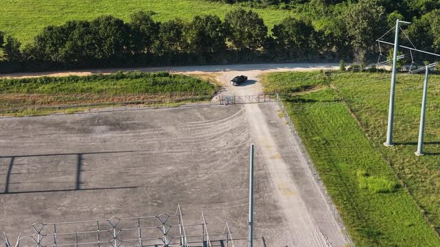 Electrical substation entrance with gravel access road and power lines in Gentry, Arkansas, aerial overview as truck parks at fenceline