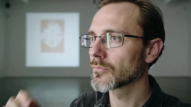 Reacting to bright projected slide, speaker dark shirt shielding eyes, adjusting glasses