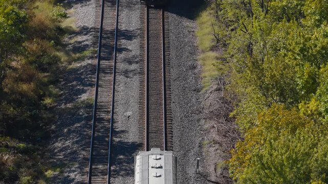 White freight railcar traveling by parallel tracks and autumn trees in Arkansas, drone backdrop as conductor approaches with steam rising
