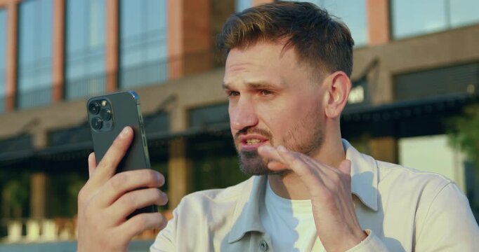 Close-up of smiling young man in white shirt standing on a city street talking on the video call, outdoors