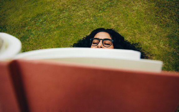 The woman enjoys reading on grass with a book in the park