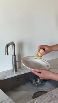 Woman washing a dirty plate with sponge at kitchen sink