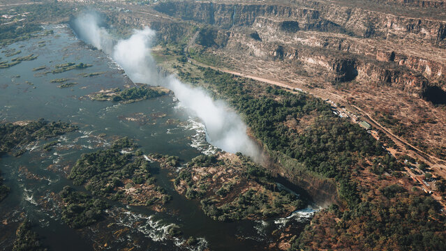 Aerial view of Victoria Falls with mist rising from the Zambezi River, lush forest vegetation, and rugged basalt cliffs in Victoria Falls, Matabeleland North Province, Zimbabwe.