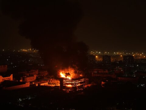 Aerial view of a large industrial building engulfed in flames at night with thick black smoke rising into the dark sky at the Chattogram EPZ in Chittagong, Chittagong Division, Bangladesh.