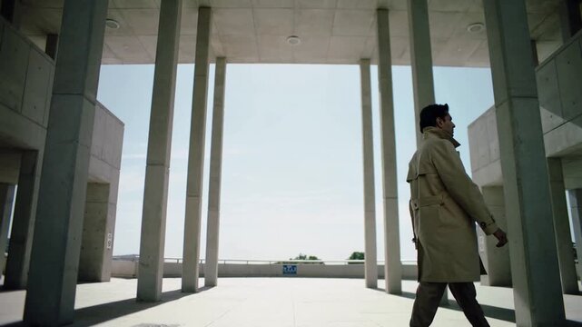 Walking man in trench coat entering from left, crossing colonnade passing columns, heading to work