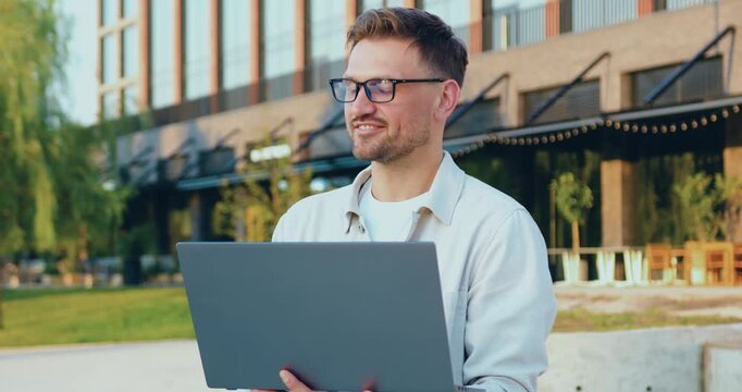 Portrait of a senior professional man working on a laptop outdoors, smiling with confidence as he types and analyzes data on the screen.