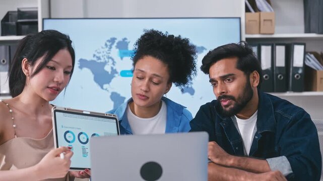 Three professional colleagues looking at a laptop screen together, discussing project details during an online video conference with a client.