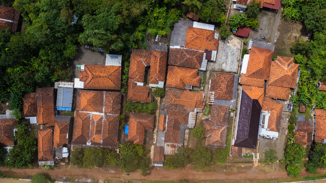 Aerial view of residential houses with orange-tiled roofs nestled among lush green trees and vegetation in Indramayu, West Java, Indonesia.
